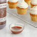 A cupcake with white frosting and a bottle of Nielsen Massey No Sugar Added Pure Vanilla Extract on a metal rack.