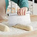 A person using a Choice stainless steel dough cutter to measure dough on a counter.