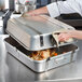 A woman using a Vollrath aluminum roasting pan to cook a large chicken.