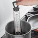 A person using an AvaTemp candy/deep fry thermometer in a pot of liquid.