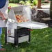 A man using a Backyard Pro Cajun Seafood Boiler Cart to cook food on a table outdoors.