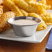 A plate of fried chicken wings and french fries with GET stainless steel ramekins of dipping sauce on a table.