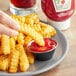 A person dipping french fries into Heinz Organic Ketchup on a plate.