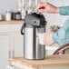 A person pouring coffee into a Bunn stainless steel coffee airpot.