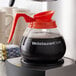 A WebstaurantStore coffee decanter with a red handle and black lid.