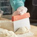 A person using a Choice stainless steel dough cutter with a wood handle to cut dough on a counter.