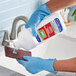 A person in blue gloves pouring Comet Creme Deodorizing Cleanser into a sponge to clean a sink.