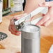 A person using a Swing-A-Way handheld can opener with a white handle to open a can.