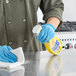 A person in blue gloves spraying Mr. Clean Lemon Zest All-Purpose Cleaner on a metal counter.