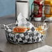 A basket with a hamburger and fries on a table lined with black and white check deli wrap.