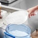 A hand using a white Choice plastic scoop to pour ice into a clear container.