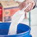 A person pouring Tide Professional Floor and All-Purpose Cleaner Concentrate powder into a blue bucket.