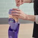 A hand holding a purple Swiffer WetJet wood floor cleaner solution refill container.