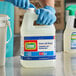 A person in blue gloves holding a white jug of Comet bleach cleaner.