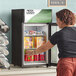 A woman opening the swing door of an Avantco countertop display refrigerator.
