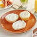 A plate of food with a bagel and eggs with a bowl of garlic and herbs cream cheese on a wood table.