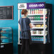 A woman standing in front of an Avantco black refrigerated air curtain merchandiser.