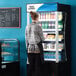 A woman standing in front of a black Avantco refrigerated air curtain display case.