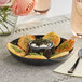 A black plastic circular dip tray with food and a spoon on a table.