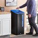 A man standing next to a black Rubbermaid Sustain mixed recycling bin.