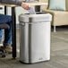 A man sitting at a desk next to a Rubbermaid stainless steel slim trash can with a plastic bag inside.