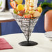 A black metal cone shaped fruit basket filled with yellow food.