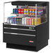 A black Turbo Air horizontal refrigerated open curtain merchandiser filled with a variety of canned drinks.