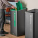 A person putting a green compost bin into a black Rubbermaid Sustain waste container.