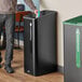 A person putting garbage in a black Rubbermaid Sustain single stream landfill trash can.