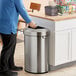 A man opening a Rubbermaid stainless steel half round waste container in a kitchen.