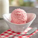 A bowl of pink ice cream with Oringer Seedless Strawberry Puree Hard Serve Ice Cream Base on a table with a spoon.