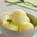 A bowl of yellow lemon sorbet with a scoop of lemon sorbet and a lemon slice.