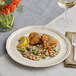 An Acopa Condesa porcelain plate with food and a glass of wine on a white background.