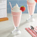 Two glasses of pink milkshakes with straws and a strawberry on top.