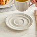 A hand holding an Acopa Condesa warm gray porcelain saucer with a cup of coffee over a plate of food.