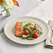 An Acopa Condesa warm gray porcelain plate with salmon and vegetables on a table.