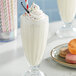 A glass of Oringer vanilla milkshake with sprinkles on top and a cookie on the side.