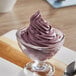 A glass bowl of purple ice cream with a spoon in it.