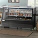 An Avantco 84" black square glass refrigerated double-duty deli case with meat and cheese on display.