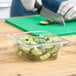 A person cutting cucumbers in a Cambro clear plastic food pan.