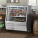An Avantco stainless steel refrigerated double-duty deli case with a glass display filled with meat and cheese.