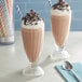 Two glasses of Oringer chocolate milkshake with straws and a spoon.