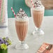 Two glasses of Oringer chocolate milkshakes with whipped cream and chocolate sprinkles on a table.
