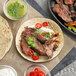 A plate of grilled steak tacos with red peppers and green sauce next to a tortilla.