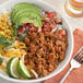 A bowl of taco meat with corn, avocado, and lime.