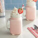 A glass mug of pink Oringer strawberry milkshake with whipped cream and a strawberry on top.