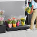 A person carrying a bunch of flowers in a plastic bag over a pink MasonWays plastic display base.