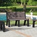 A set of brown Malibu-style benches with black legs on a sidewalk with grass.