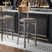 Two Lancaster Table & Seating Boomerang bar stools with taupe vinyl seats and vintage wood backs at a bar counter.