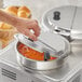 A person's hand holding a Choice stainless steel inset cover over a pot of food.